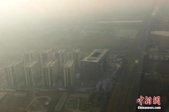 　　12月16日，透過(guò)飛機(jī)舷窗俯瞰北京，城市建筑隱在霧霾中。12月15日北京發(fā)布今年首個(gè)空氣重污染紅色預(yù)警：16日20時(shí)，北京市啟動(dòng)空氣重污染紅色預(yù)警。中新社記者 盛佳鵬 攝